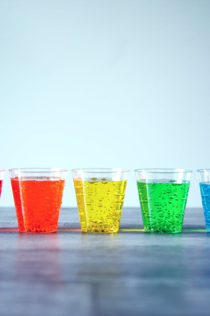 Five colorful fizzy drinks in plastic cups organized in a row indoors.