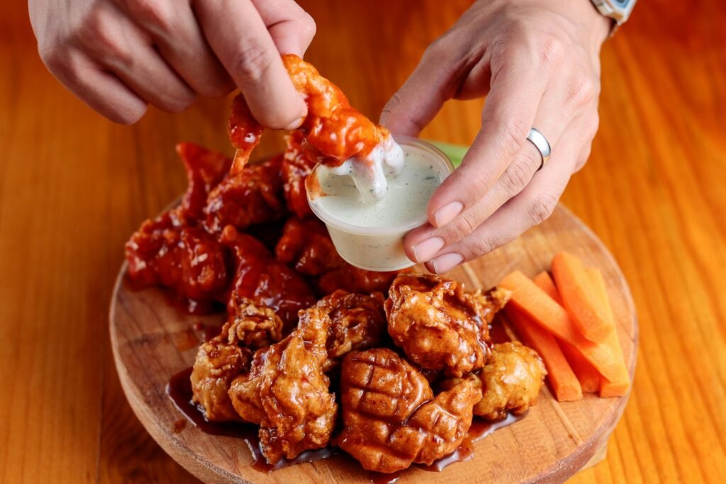 pexels-photo-24182617-24182617 Delicious chicken wings on a wooden platter with dipping sauce and carrot sticks.