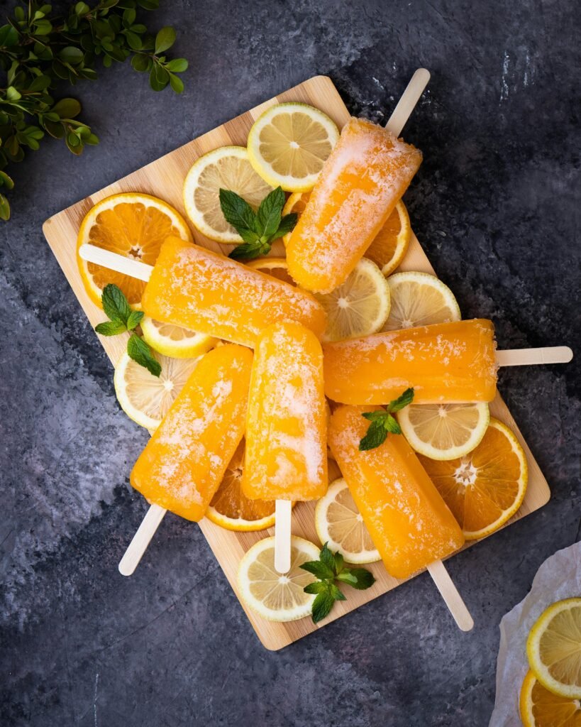 Bright citrus ice pops arranged with lemon and orange slices on a wooden tray. Perfect summer treat.