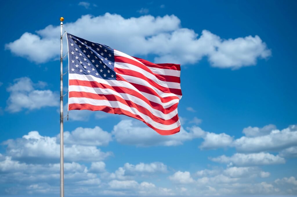 Vibrant American flag flying with a bright blue sky and fluffy clouds in the background.