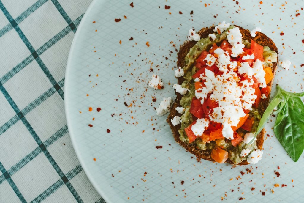 Top view of avocado toast with feta and tomato on a light plate with a checkered tablecloth.