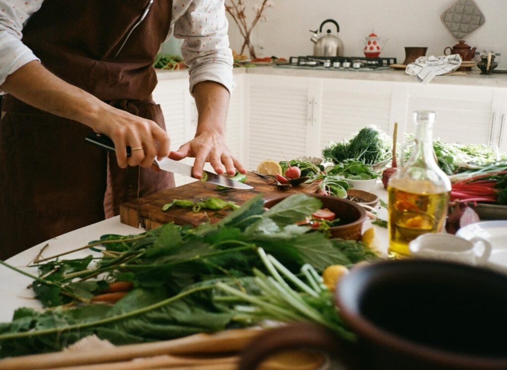 Adult preparing a fresh vegetable salad in a cozy kitchen with various ingredients and kitchenware.