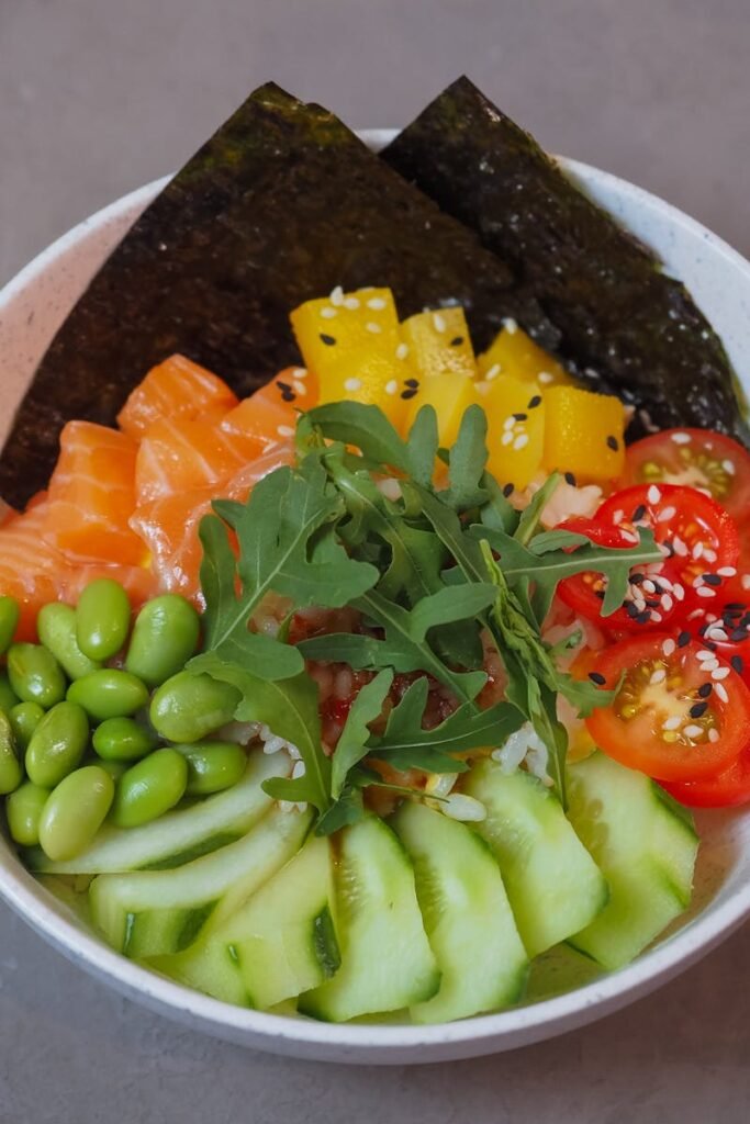 Close-up of a vibrant poke bowl with fresh veggies, salmon, and seaweed on a neutral background.