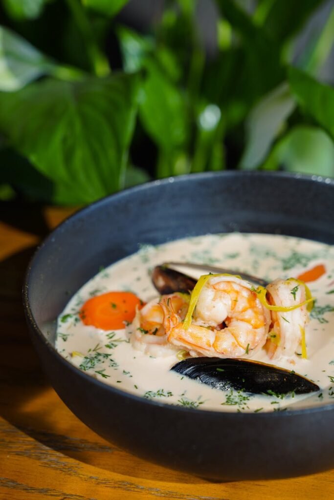 Close-up of creamy seafood chowder with shrimp and mussels in a black bowl.