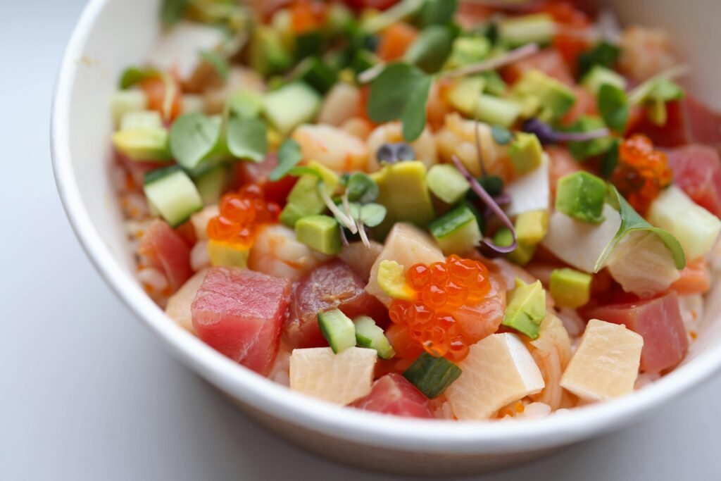 A vibrant poke bowl featuring fresh fish, avocado, cucumber, and roe in a white bowl.