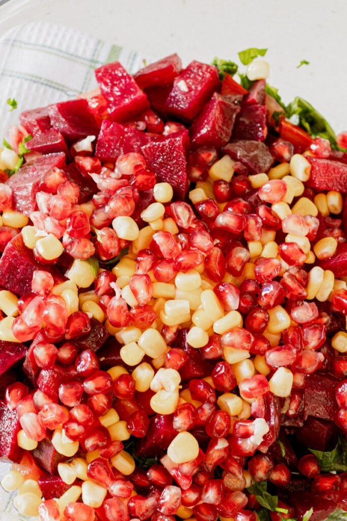 Colorful salad with pomegranate, corn, and beets in a glass bowl.