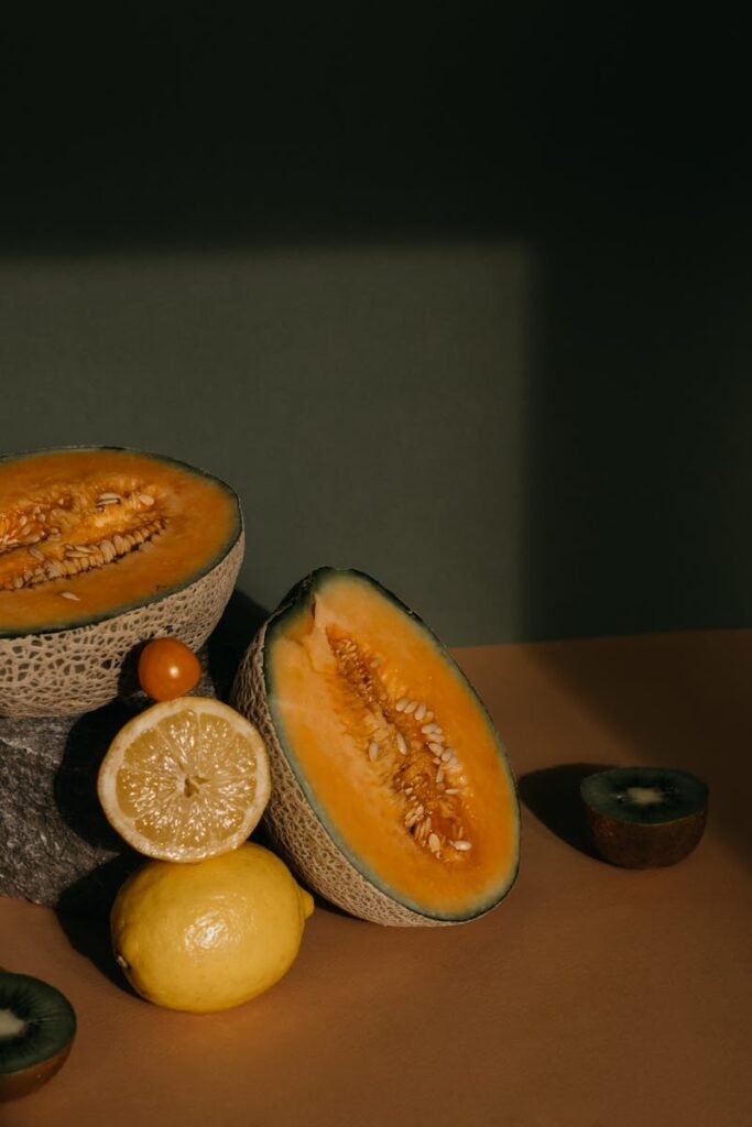 A variety of fresh fruits including sliced melon, lemon, and kiwi on a rustic table setting.