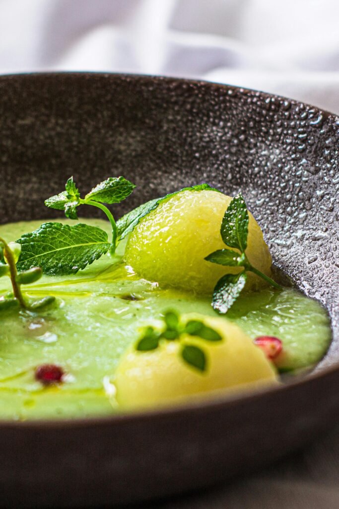 A vibrant green melon soup garnished with fresh mint leaves in a textured bowl.