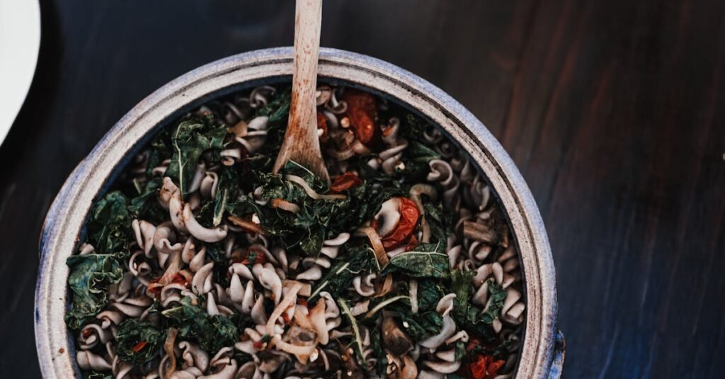 Top view of appetizing fusilli mixed with spinach leaves and sun dried tomatoes in bowl with wooden spatula