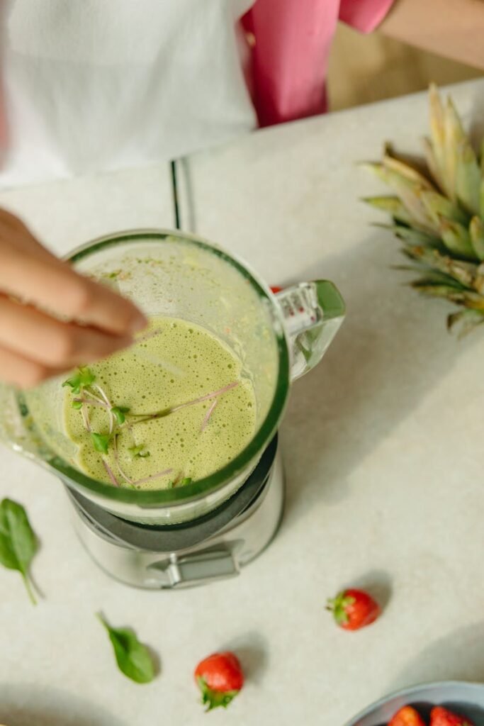 Top view of a green smoothie being prepared with pineapple and greens on a countertop.